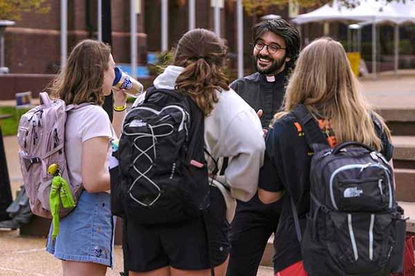 A young Jesuit wearing a priest’s collar speaks to students in the plaza close to the clock tower.